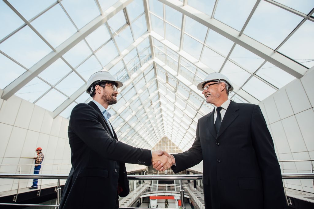 two cheerful businessman handshaking helmet new building